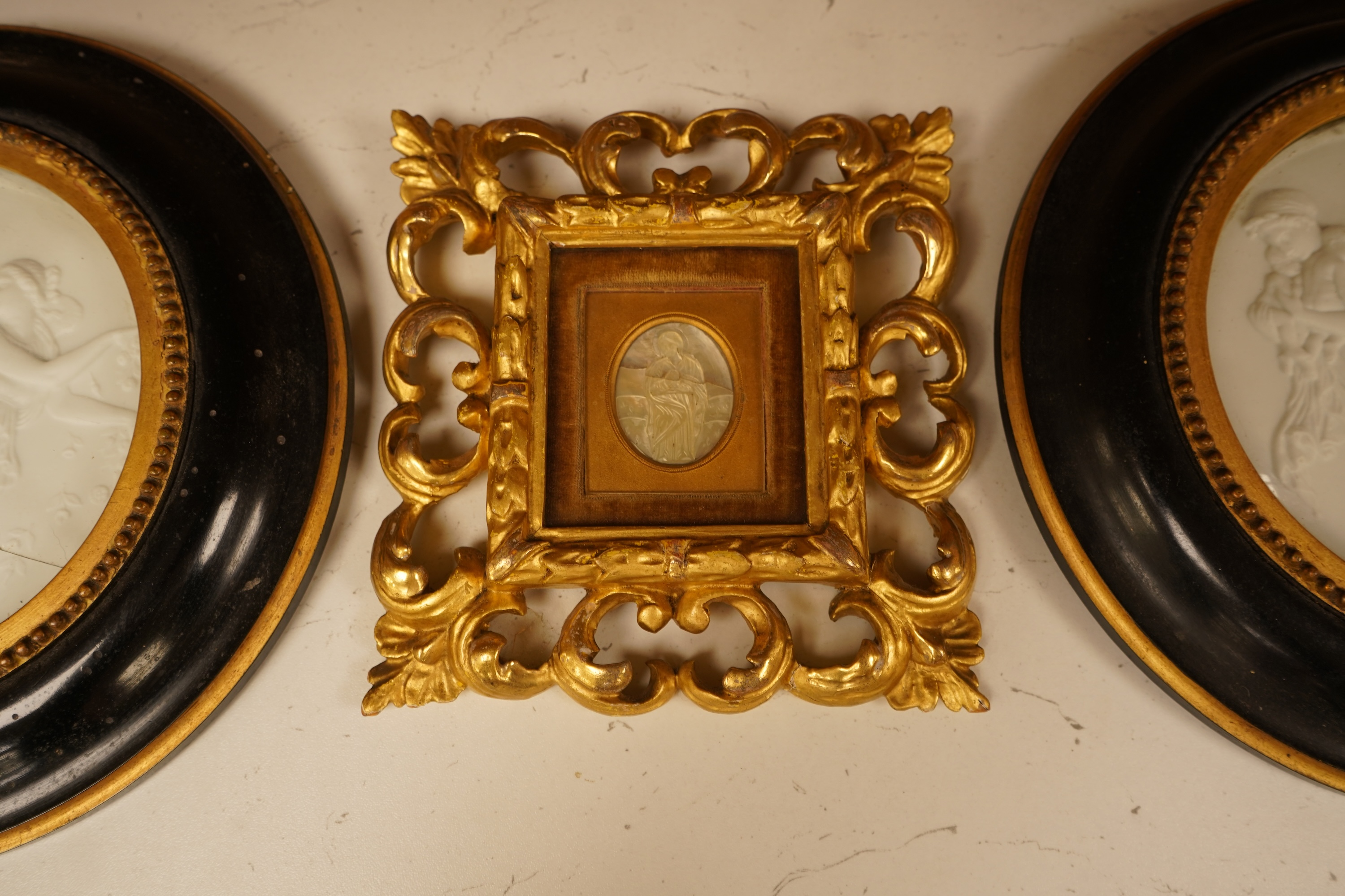 A late 19th century mother of pearl plaque of a saint, housed in a gilt wood florentine frame, together with a pair of Copenhagen biscuit porcelain plaques of Night and Day after Thorvaldsen, in convex frames